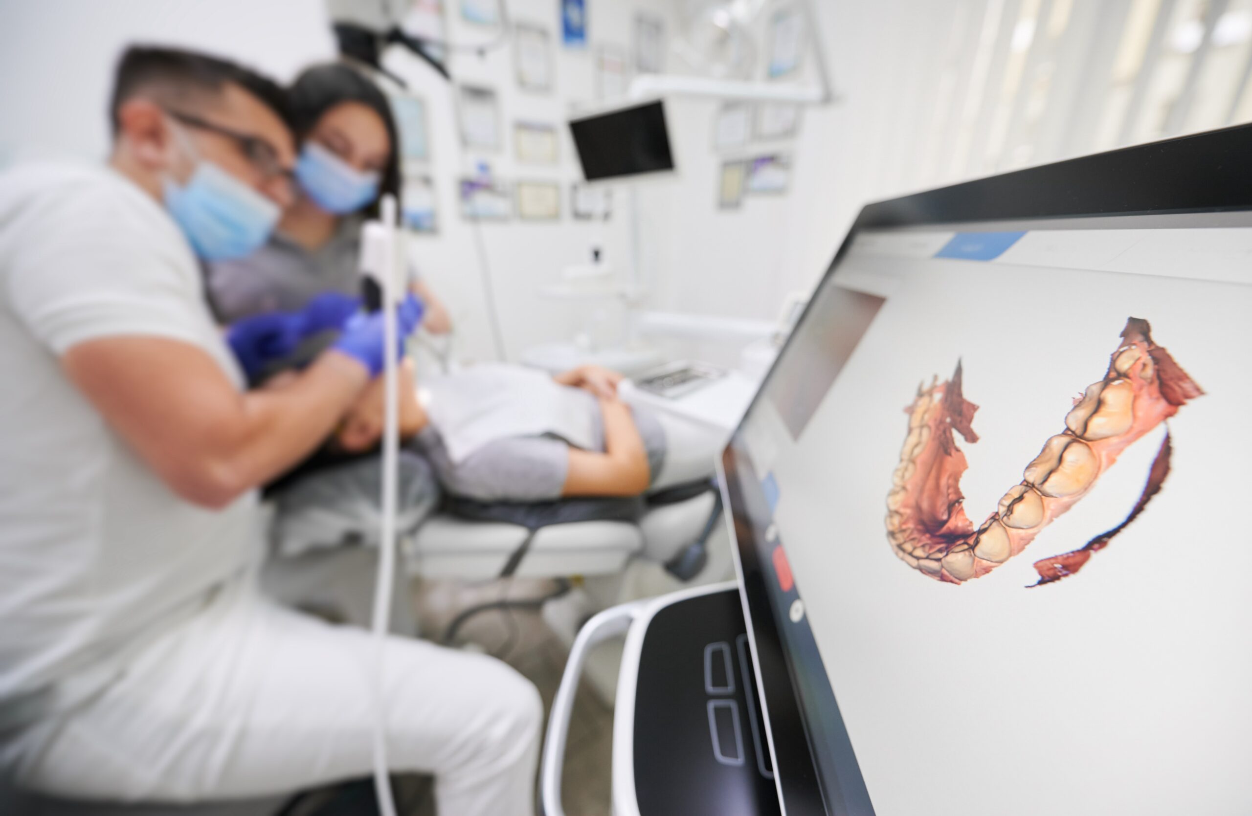 Dental professionals review a 3D tooth scan on a monitor during a patient's visit