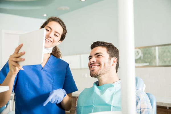 Dentist shows a happy male patient his smile reflection in a tablet