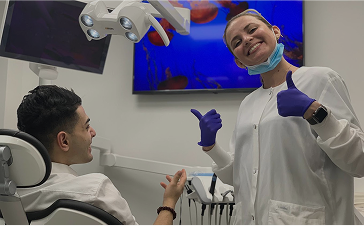 Smiling dental professional gives thumbs up next to patient