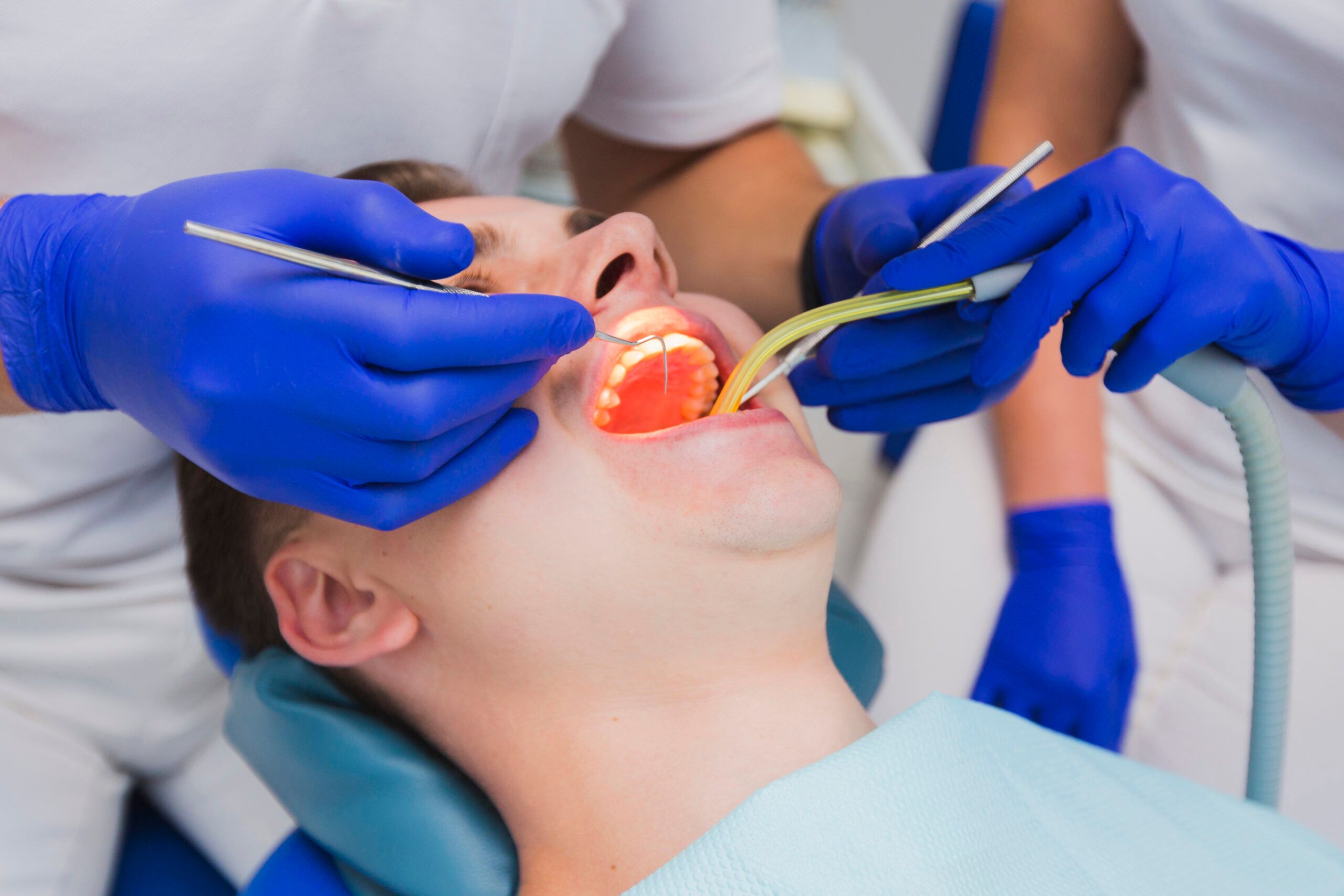 Two dentists work on a patient's open mouth with illuminated tools